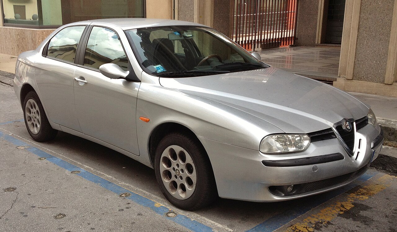 Ασημένιο Alfa Romeo 156 σταθμευμένο σε δρόμο με μπλε γραμμές.