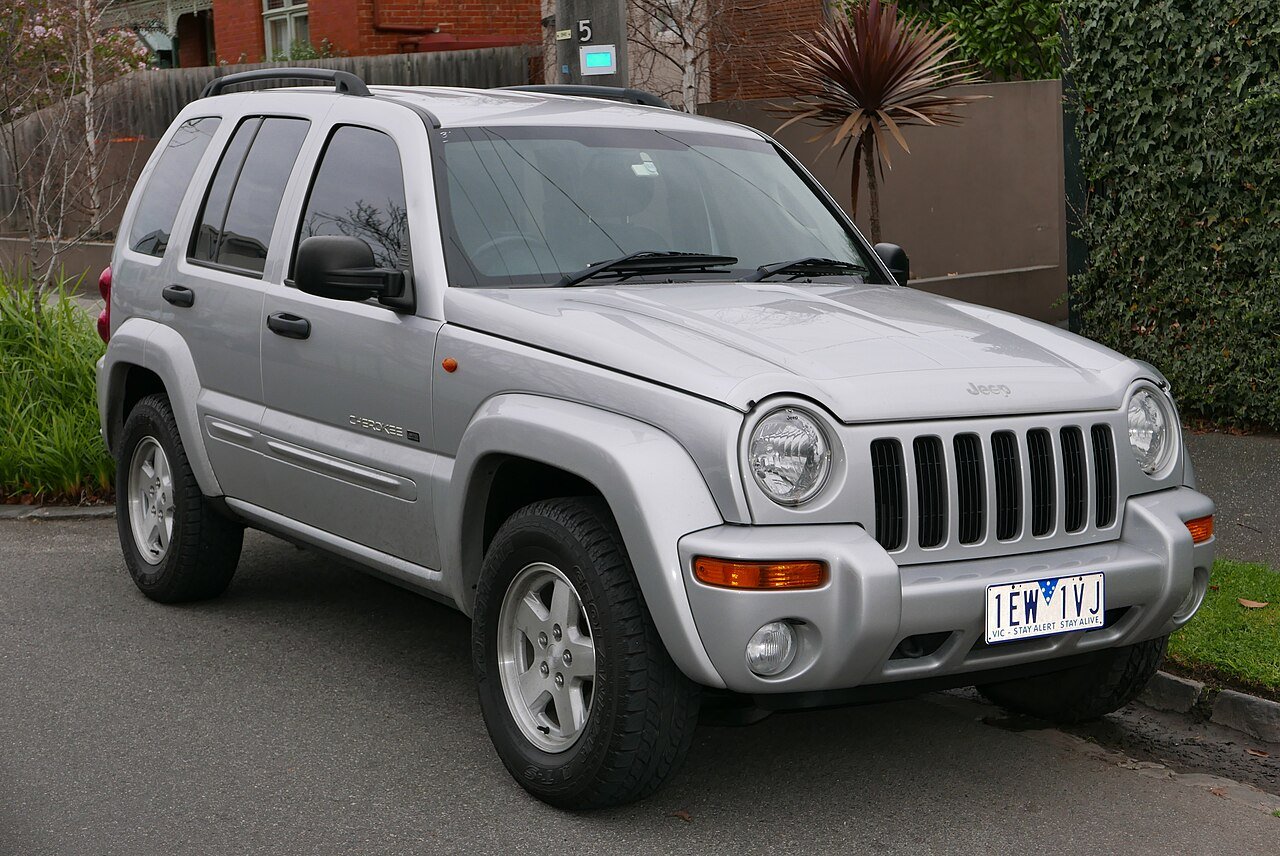 Ασημί Jeep Cherokee σταθμευμένο σε δρόμο, με φόντο κτίρια.
