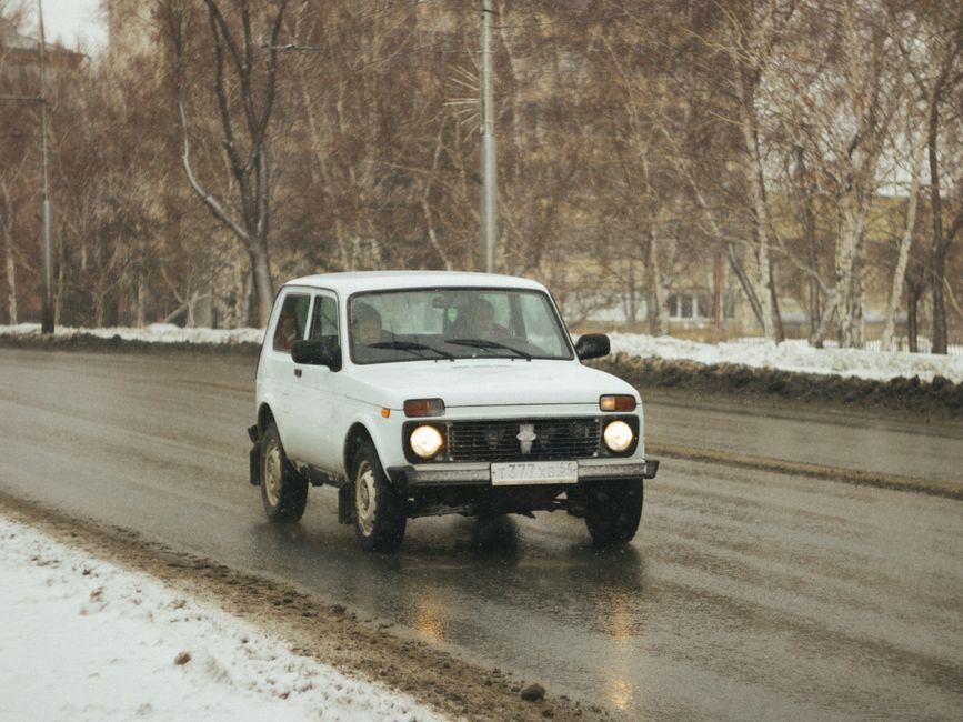 Λευκό Lada Niva οδηγεί σε βρεγμένο δρόμο με χιόνι.