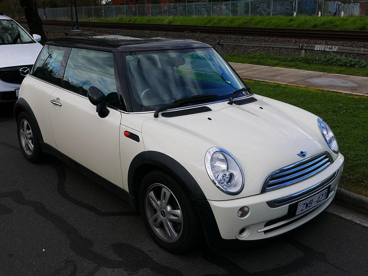 Λευκό Mini Cooper σταθμευμένο δίπλα σε σιδηροδρομικές γραμμές.