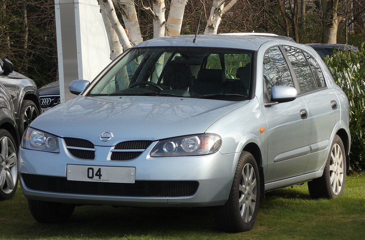 Ασημί Nissan Almera, μοντέλο hatchback, παρκαρισμένο σε γρασίδι.