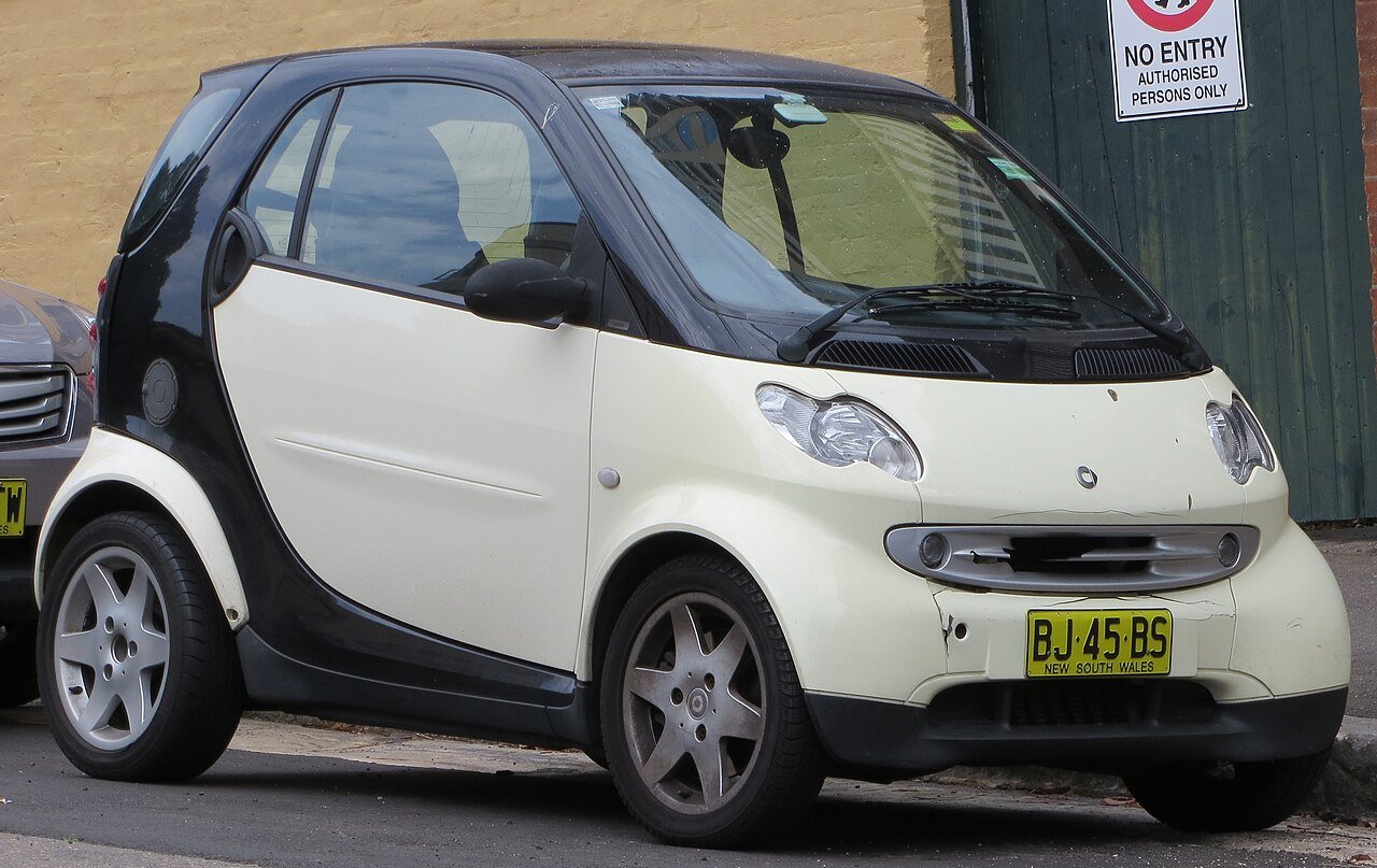Ένα λευκό Smart Fortwo παλιάς γενιάς παρκαρισμένο στο δρόμο.