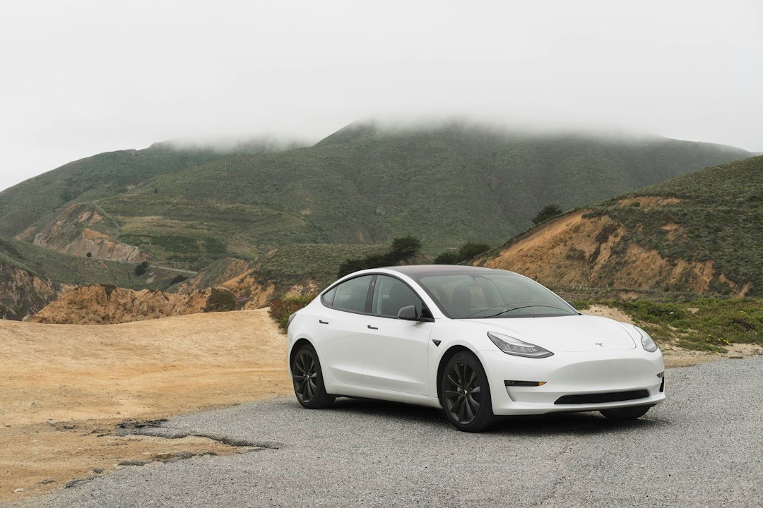 Λευκό Tesla Model 3 παρκαρισμένο σε δρόμο με βουνά στο βάθος.